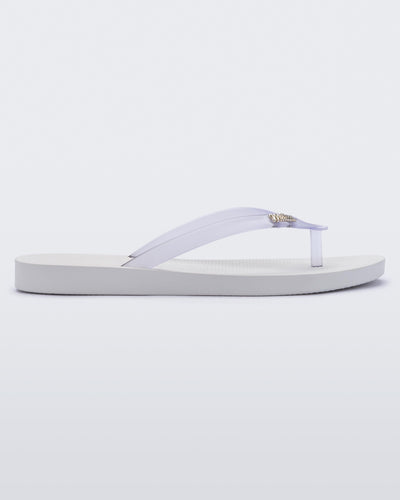 An outter side view of a white/clear Melissa Sun Venice flip flop with a white sole and clear straps with "melissa" on one strap.