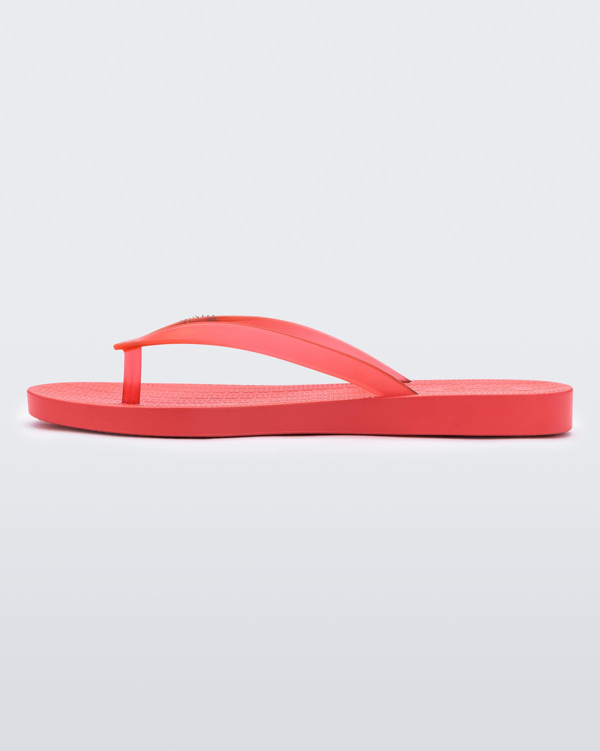An inner side view of a red Melissa Sun Venice flip flop with a "melissa" logo on the strap.