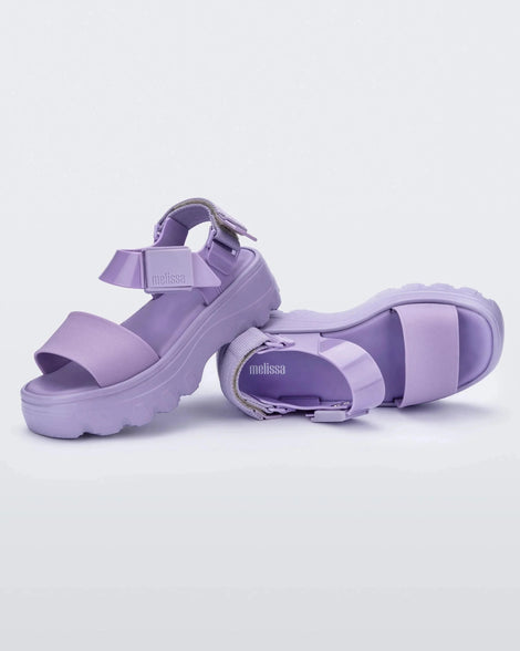 Angle view of a pair of Melissa Kick Off platform sandals in lilac. The sandal has an ankle strap with a plastic clasp closure on the front ankle side, additional velcro adjustable strap is on the back of the ankle strap. 